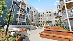 A modern apartment complex with a spacious courtyard and wooden benches.