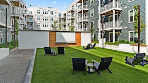 A modern outdoor seating area with black chairs and tables is surrounded by apartment buildings.