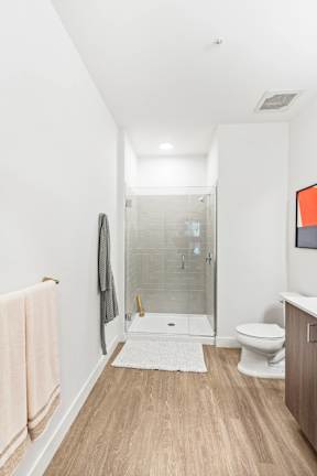 A bathroom with a toilet, a sink, a towel, and a glass shower stall.