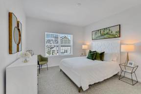 A bedroom with a large bed, a chair, and a painting on the wall.