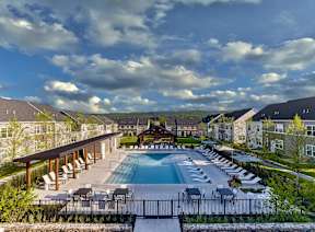 A large outdoor swimming pool surrounded by lounge chairs and a wooden pavilion.
