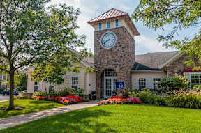 Exterior view of Pennbrook Station Apartments in Lansdale, PA, featuring landscaped gardens and a clock tower.