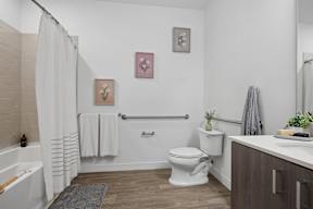 A white toilet sits in a bathroom with a white tub and a white shower curtain.