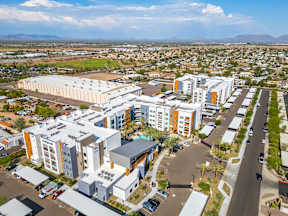 A large white building with a grey roof is surrounded by other buildings and cars.