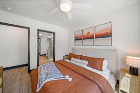 A bedroom with a bed, a ceiling fan, and a painting on the wall.