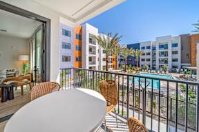 A balcony with a table and chairs overlooks a pool and buildings.