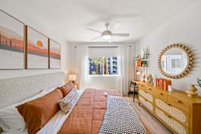 A bedroom with a large bed, a ceiling fan, and a painting of a sunset on the wall.