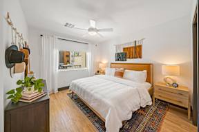A bedroom with a large bed, a ceiling fan, and a wooden nightstand.