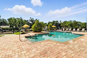 A pool surrounded by a brick patio and trees.