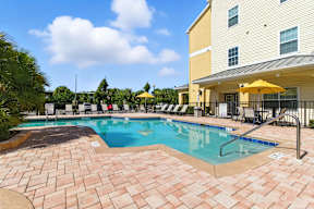 A large outdoor swimming pool surrounded by a brick patio and lounge chairs.
