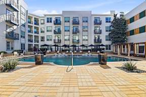 A swimming pool surrounded by a tiled patio and apartment buildings.