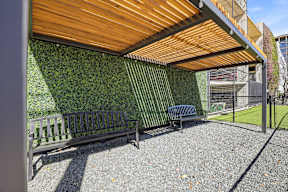 A wooden bench sits under a wooden roof next to a green wall.