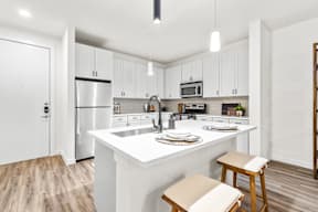 A kitchen with white cabinets and a white island with two stools.