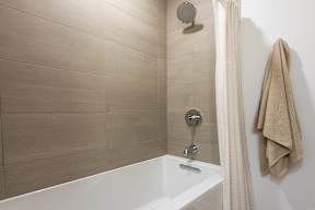 A white bathtub with a shower head and a towel hanging on the wall.