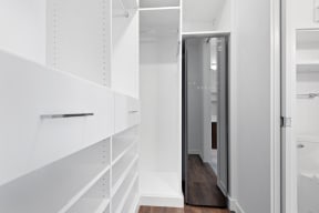 a walk in closet with white shelves and a glass door