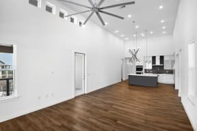 a living room with white walls and a kitchen with a ceiling fan