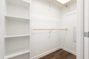 a walk in closet with white shelves and a wood floor
