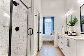 A bathroom with a marble shower and white cabinets.
