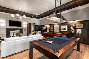 A pool table with a black cloth and a white couch in the background.