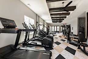 A black treadmill is in a spacious gym with a checkered floor.