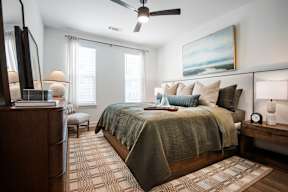 A bedroom with a bed, a dresser, a ceiling fan, and a painting on the wall.