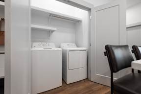 A laundry room with a washer and dryer and a chair.