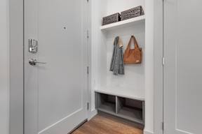 A white door with a silver handle and a white shelf with a bag and a jacket hanging on it.