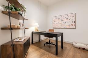 A room with a desk, chair, and a shelf with a plant on it.