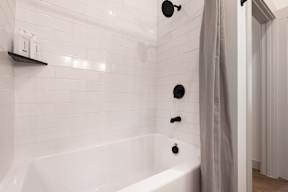 A white tiled bathroom with a white bathtub and a grey shower curtain.