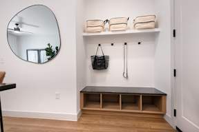 A bathroom with a round mirror, a bench, and a black bag hanging on the wall.