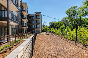 A row of modern apartment buildings with a fenced in dirt area in front.