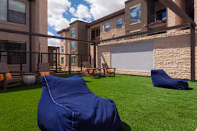 A blue bean bag chair sits on a lawn in front of a building.