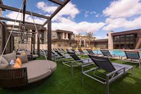 A sunny day at the poolside with lounge chairs and a hanging chair.
