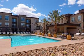 A swimming pool is surrounded by chairs and palm trees in front of a building.