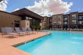 A swimming pool in front of a building with lounge chairs around it.