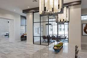 A modern chandelier hangs over a marble table in a spacious lobby.