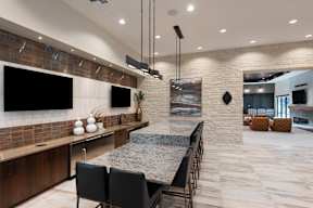 A modern kitchen with a long island and black chairs.