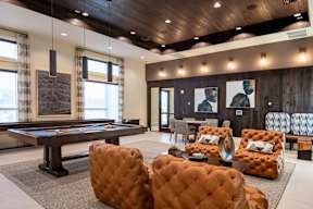A room with a pool table and leather chairs.