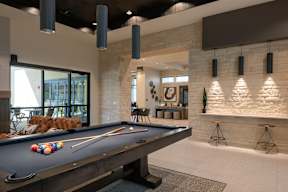 A pool table is in the middle of a room with a stone wall.