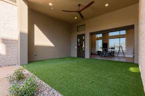 A patio with a green lawn and a ceiling fan.