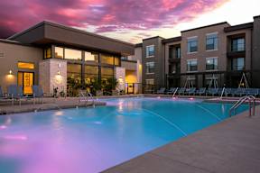 A swimming pool in front of a building with a sunset in the background.