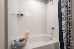 A white bathtub with a shower curtain and a shelf above it.