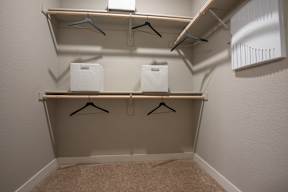 A small closet with two shelves and three hangers.
