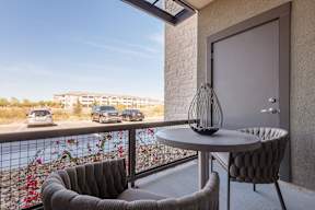 A balcony with a table and two chairs overlooking a parking lot.