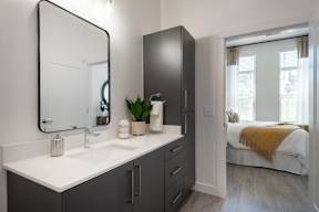 A bathroom with a sink, mirror, and a bedroom in the background.