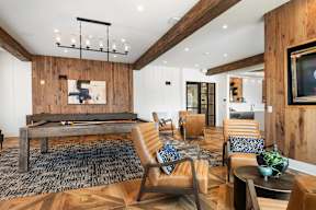 A modern living room with a pool table and leather chairs.
