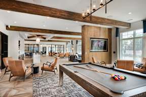 A billiard table is in the middle of a room with leather chairs.