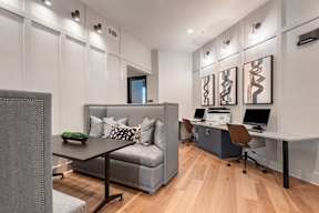 A modern office with a grey couch and a desk with a laptop and a monitor.