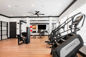 A gym with a row of treadmills and a ceiling fan.