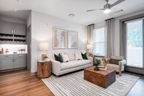 A modern living room with a white sofa, wooden coffee table, and a large window with curtains.